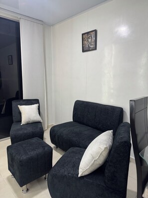 Un salon moderne avec un canapé aux couleurs sombres, un petit pouf et une œuvre d’art encadrée accrochée au mur.