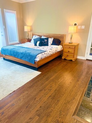 A bedroom with a wooden bed, two bedside tables with lamps, a white rug, and a wooden floor. - King Room • Self Check-in • 2 min to Transit (Mississauga)