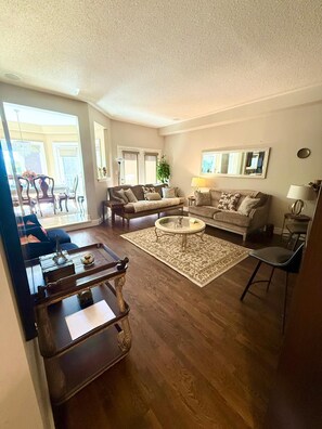 Un salon comprenant un canapé, deux fauteuils, une table basse et un coin repas agrémenté d’un lustre.