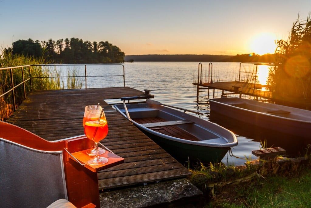 A wooden dock with a glass of drink, a boat, and a bench.