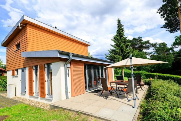 Uma casa moderna de dois andares com um alpendre com móveis de exterior e uma mesa.