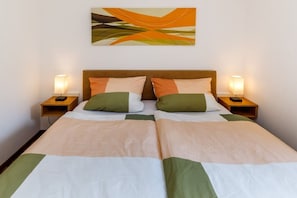 Uma cama de casal com cabeceira de madeira, duas mesas de cabeceira com abajures e um quadro abstrato pendurado na parede.