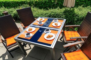 An outdoor dining area with a table set for four, surrounded by wicker chairs with orange cushions. - Hans am See with private jetty (Schwerin)