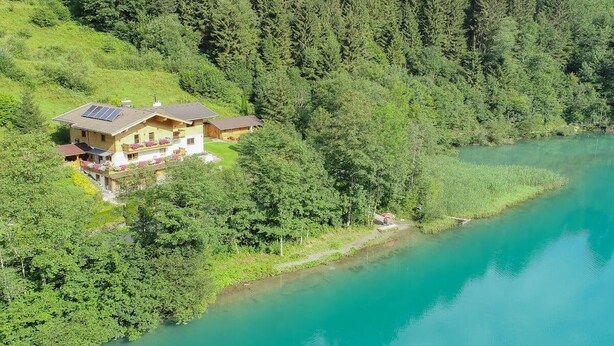 Una casa con un panel solar, rodeada de un bosque denso y un lago.