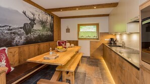Un interior rústico con una mesa de madera, bancos, una zona de cocina y un mural con ciervos en la pared.