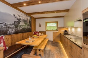 A rustic interior with a wooden dining table, benches, a kitchen area, and a mural of deer on the wall. - Holiday apartment with 1 bedroom (Kaprun)