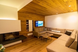 A modern living room with a fireplace, a sectional sofa, a coffee table, and a television mounted on the wall. - Cabin in Uttendorf with swimming pool (Uttendorf)