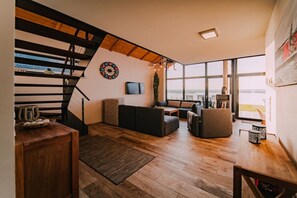 A modern living room with a staircase, a television, and a large window offering a view. - Holiday home in Löbnitz with swimming pool (Löbnitz)