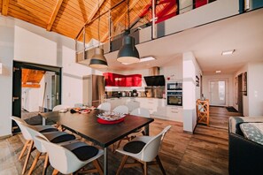 Una cocina moderna con armarios blancos, un protector contra salpicaduras rojo y un comedor con mesa de madera y sillas blancas.