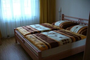 A double bed with a patterned bedspread and pillows, a wooden headboard, and a window with sheer curtains. - Holiday apartment with 2 bedrooms (Sassnitz)