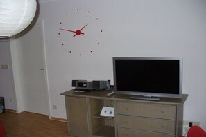 A room with a flat-screen TV on a cabinet, a clock on the wall, and a door in the background. - Holiday apartment with 2 bedrooms (Sassnitz)