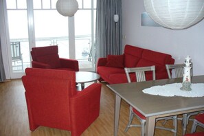 A room with a dining table, red chairs, a white tablecloth, and a view through a large window. - Holiday apartment with 2 bedrooms (Sassnitz)