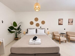 A hotel room with a large bed, a bedside table, a chair, a small table, a potted plant, and wall decor.