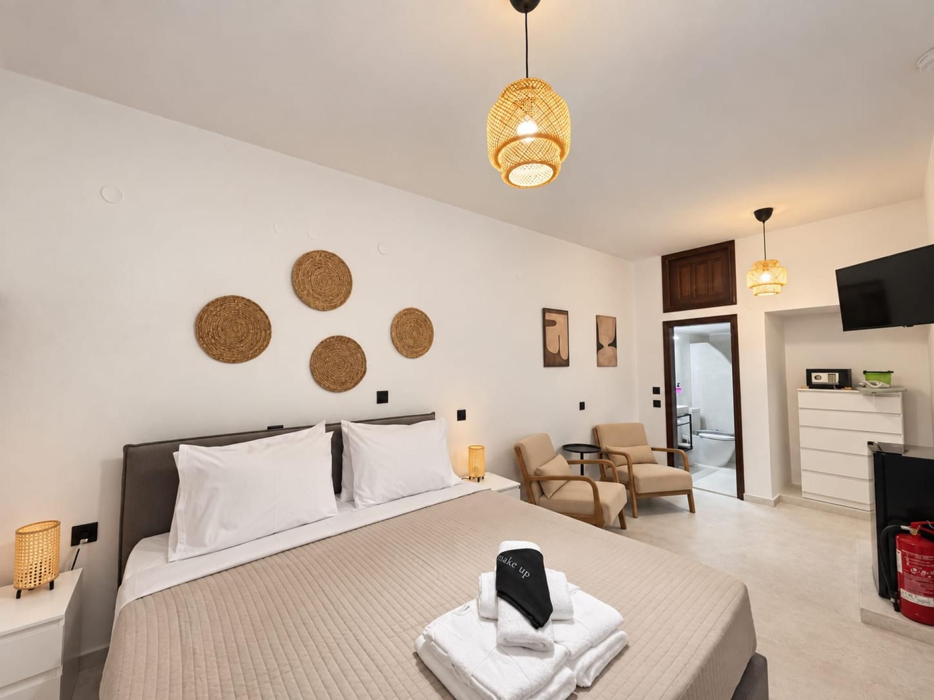 Une chambre d’hôtel avec un lit, un bureau, une chaise, une télévision et une salle de bain visible à travers une porte ouverte.