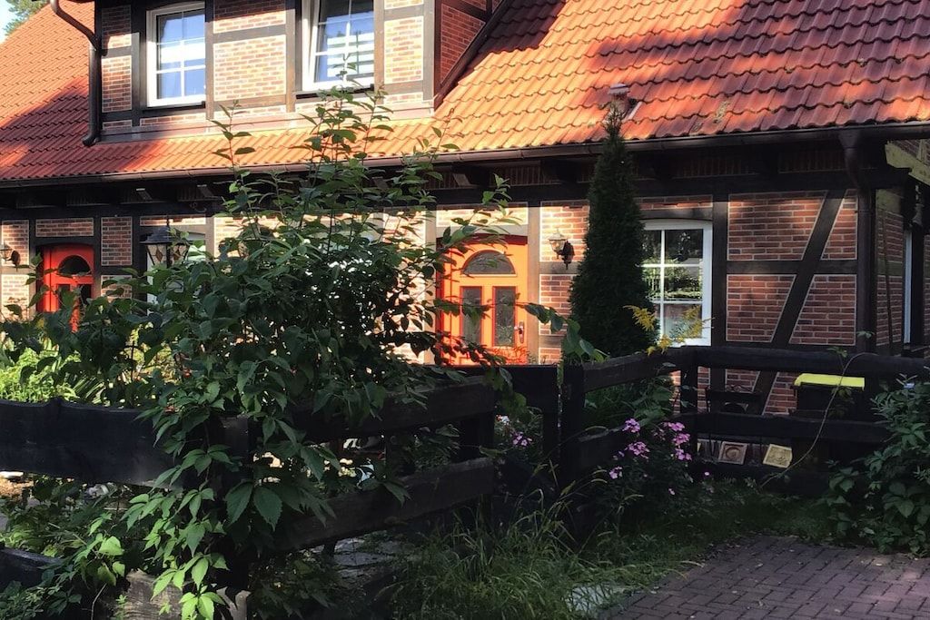 A traditional brick house with a red-tiled roof, a wooden fence, and a garden area with plants and flowers.