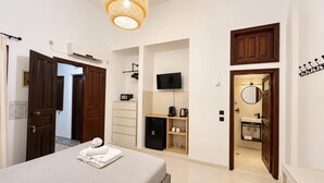 Ein Hotelzimmer mit Bett, Fernseher, einer kleinen Küchenzeile und einem Badezimmer mit Spiegel.