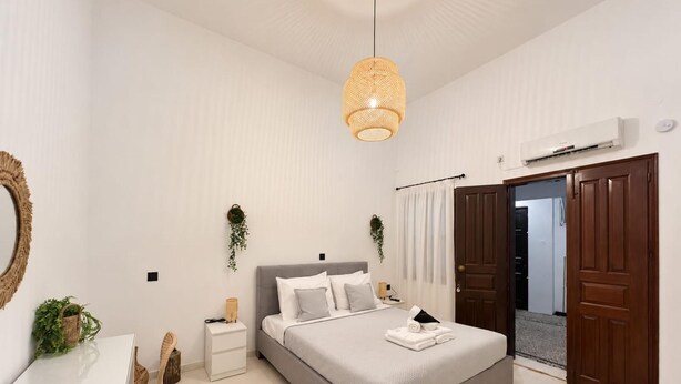 Ein Schlafzimmer mit Bett, Nachttischen, Schreibtisch, Stuhl, Pendelleuchte und einer Tür.