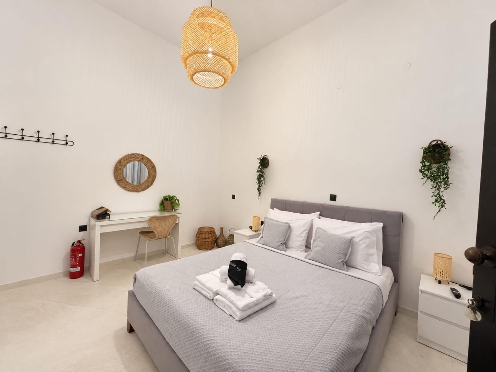 A modern bedroom with a bed, bedside tables, a desk, and a hanging plant.