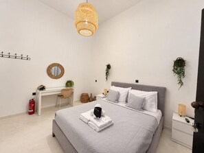 Een moderne slaapkamer met een bed, nachtkastjes, een bureau en een hangplant.