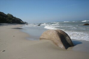 Ein Strand mit einem großen Felsen im Vordergrund und brechenden Wellen.