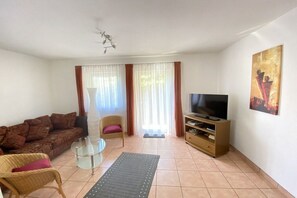 Ein Wohnzimmer mit einer Couch, Sesseln, einem Fernseher und einem Bild an der Wand.