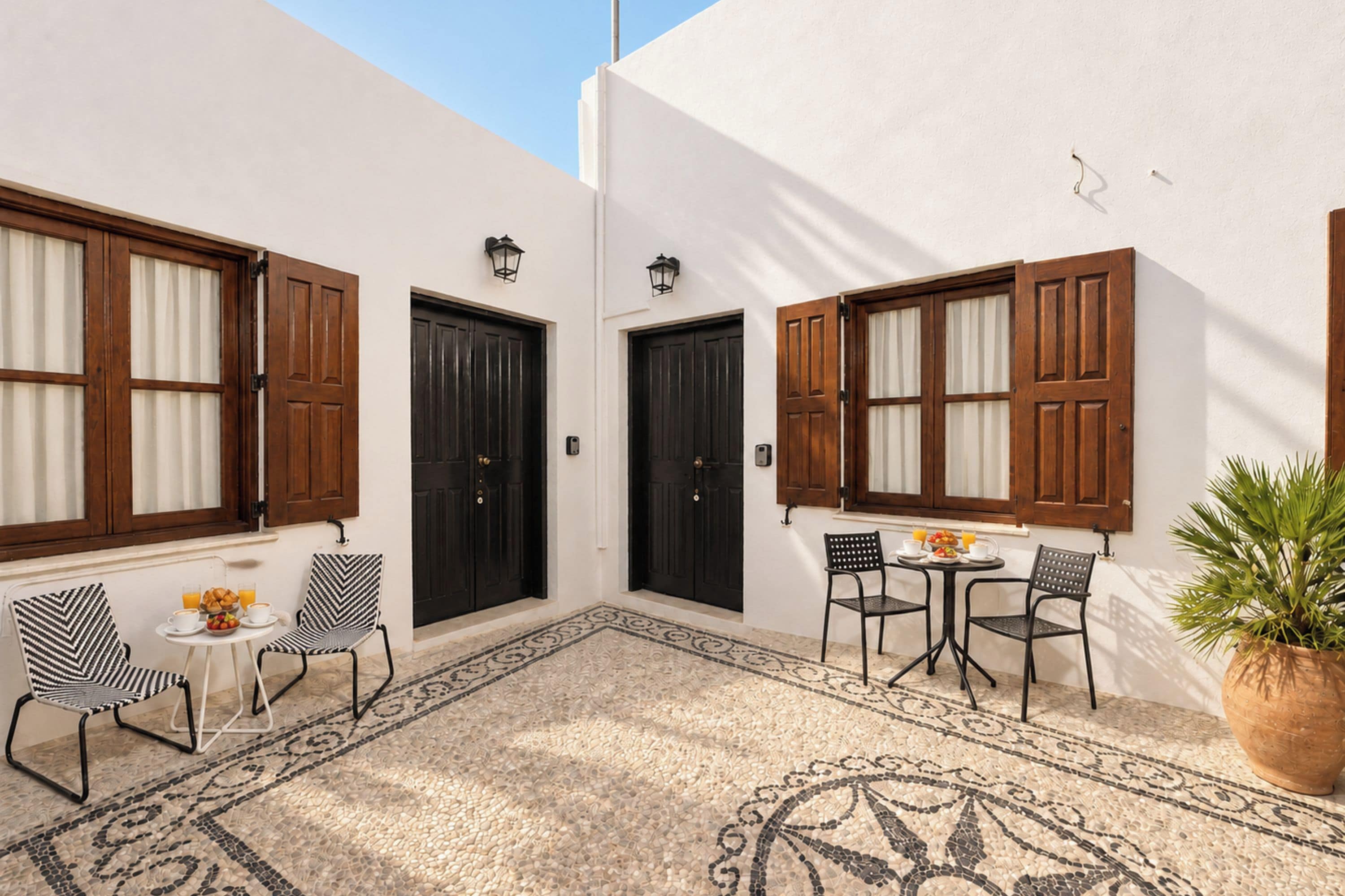 Un patio con dos puertas, una mesa y sillas, y una planta en maceta.