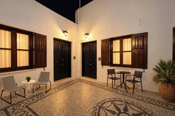 Une cour intérieure avec deux portes, une petite table, deux chaises et un pot de fleurs.