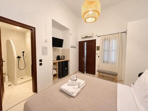 A hotel room with a bed, a shower, a television, a desk, and a bench. - Eternel Room 3 in Lindos (Rhodes)