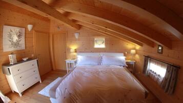 Ein Schlafzimmer mit Holzbalkendecke, einem Bett, einem Schminktisch, Nachttischen und einem Fenster mit Vorhängen.