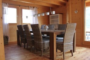 Ein Holzinterieur mit einem Esstisch, umgeben von Korbstühlen, einer Vitrine mit Glastüren und einer herzförmigen Dekoration an der Wand.