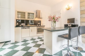 A modern kitchen with a checkered floor, a central island, bar stools, and a TV. - Apartment House Saxonia (Bad Schandau)