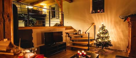 A cozy living room with a fireplace, a staircase, and a decorated Christmas tree.
