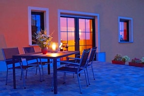 An outdoor dining area with a table and chairs, a vase with flowers, and a bottle of wine. - Holiday apartment with 2 bedrooms (Hörnitz)