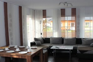 A modern living room with a sofa, a dining table set for two, and a view of the outdoors. - Holiday home Stein in the Spreewald Lübbenau (Lübbenau)