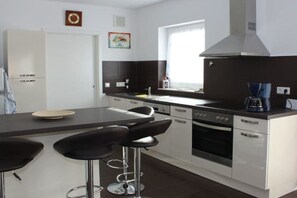 A modern kitchen with a central island, bar stools, a coffee machine, and a built-in oven. - Holiday home Stein in the Spreewald Lübbenau (Lübbenau)