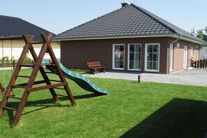 A residential building with a brick exterior, a green slide, and a wooden swing set in the yard. - Holiday home Stein in the Spreewald Lübbenau (Lübbenau)