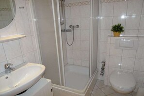 Une salle de bain avec une douche, un lavabo, des toilettes et une petite plante en pot accrochée au mur.