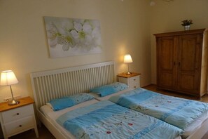 Ein Schlafzimmer mit einem Doppelbett, zwei Nachttischen mit Lampen, einem Holzschrank und einem floralen Gemälde an der Wand.