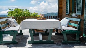 A wooden outdoor seating area with a table and benches, a view of the landscape, and a wooden structure with green shutters. - Kogljahrerhütte || Prebl (Prebl)