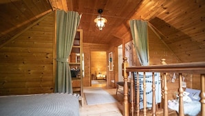 A cozy attic bedroom with a wooden ceiling, a bed, a staircase, and a view of the living area. - Kogljahrerhütte || Prebl (Prebl)
