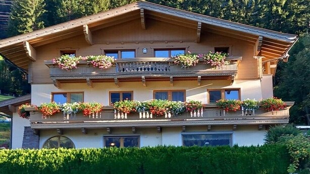 Un edificio de varios pisos con balcones decorados con flores, rodeado de vegetación.