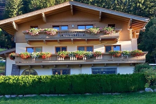 A multi-story building with balconies adorned with flowers, surrounded by greenery. - Holiday apartment with 3 bedrooms (Bramberg)