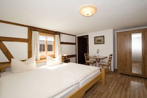 Ein Schlafzimmer mit einem Holzbett, einem Schreibtisch, einem Stuhl, einem fenster mit Vorhängen und einer Tür.