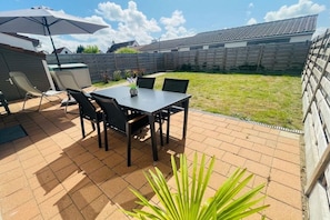En udendørs terrasse med et bord og stole, et træhegn og en græsplæne.