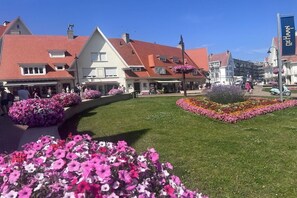 Ein Stadtplatz mit traditioneller Architektur, einem Blumenbeet und wolkenlosem, blauem Himmel.