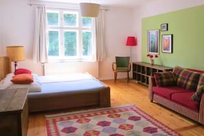 A room with a bed, a red sofa, a chair, a lamp, and a window with curtains.