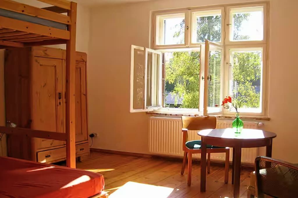 Ein Zimmer mit einem Etagenbett, einem Tisch mit Stühlen und einem Fenster mit Blick auf Bäume.