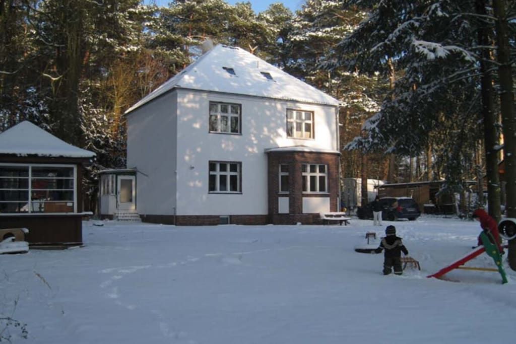 Kaksikerroksinen talo, jonka pihalla on lunta, autotalli näkyy selvästi, ja siellä on pieni leikkialue, jossa on liukumäki.