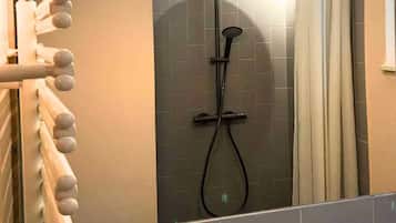 Eine Duschkabine mit Glastür, einer Handbrause und einem Handtuchhalter mit mehreren Handtüchern.