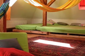 Ein Schlafzimmer im Loft-Stil mit einer Hängematte, zwei Betten, einem grünen Sofa und einem gemusterten Teppich.